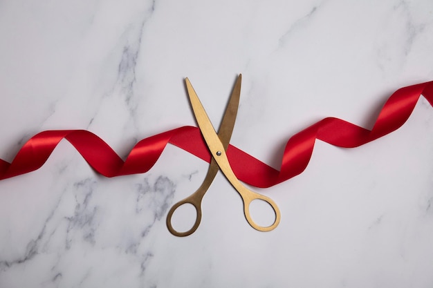 Grand opening background gold scissors with red ribbon on a marble background