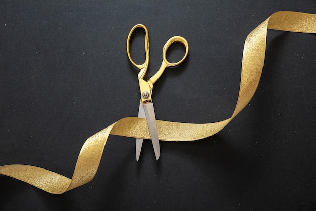 Foto grand opening forbici d'oro che tagliano il nastro di raso dorato su sfondo nero