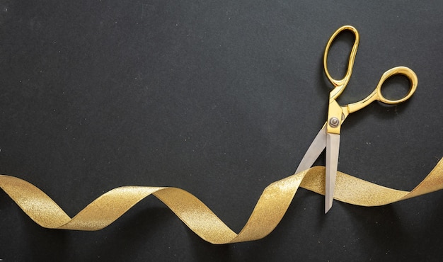 Photo grand opening gold scissors cutting gold satin ribbon black background