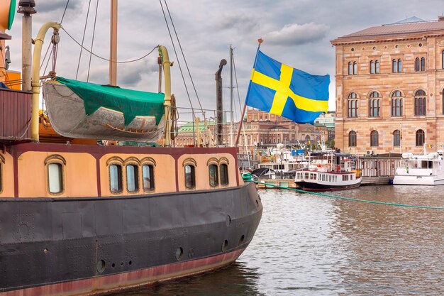 Photo a grand swedish flag flutters on a boat in a bustling stockholm harbor sweden