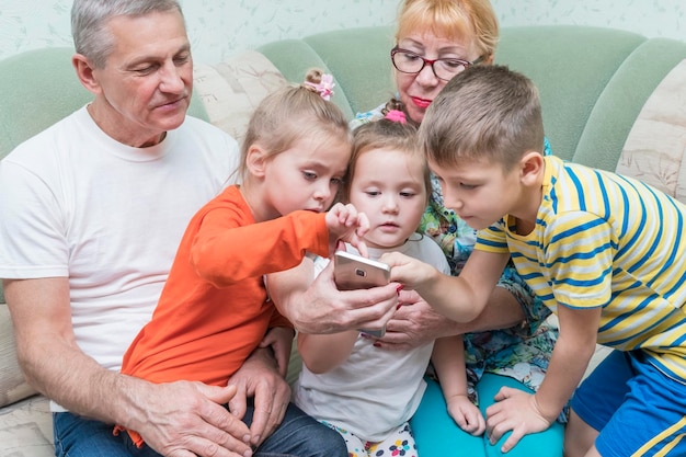 grandchildren point to the screen smart phone while sitting in the hands of grandparents