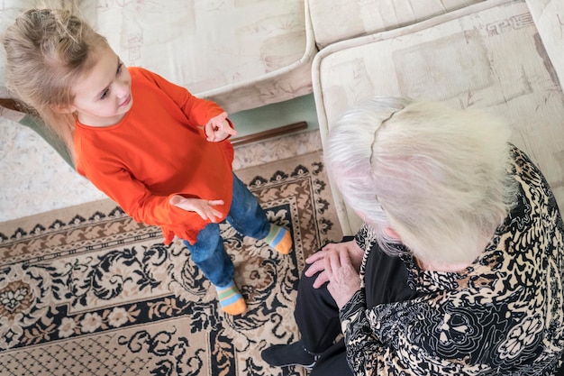 Granddaughter counting on fingers for great-grandmother sitting on the sofa, top view