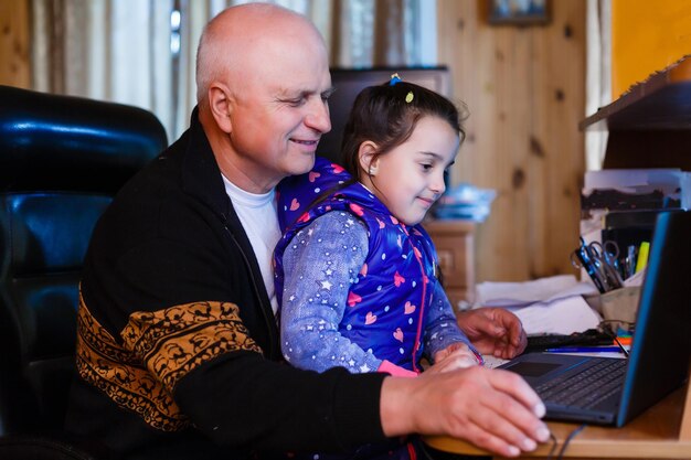 Granddaughter helping grandpa to make online communication on laptop