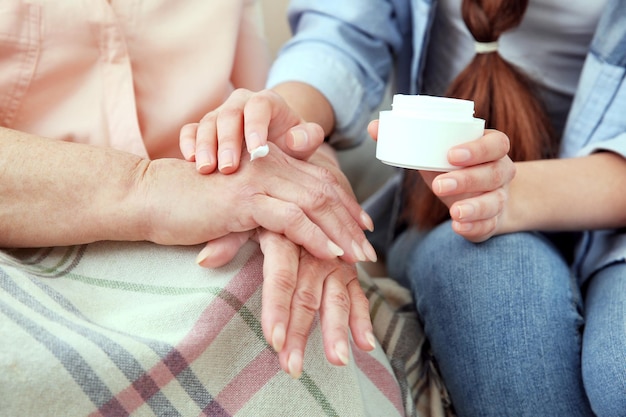 Granddaughter helping granny to apply skin cream close up