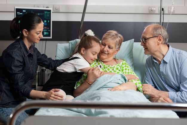 Photo granddaughter hugging sick elderly grandmother visiting her in hospital ward