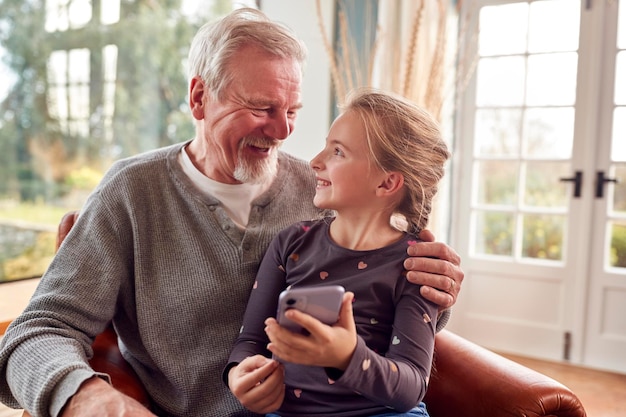 Granddaughter Showing Grandfather How To Use Mobile Phone At Home Together