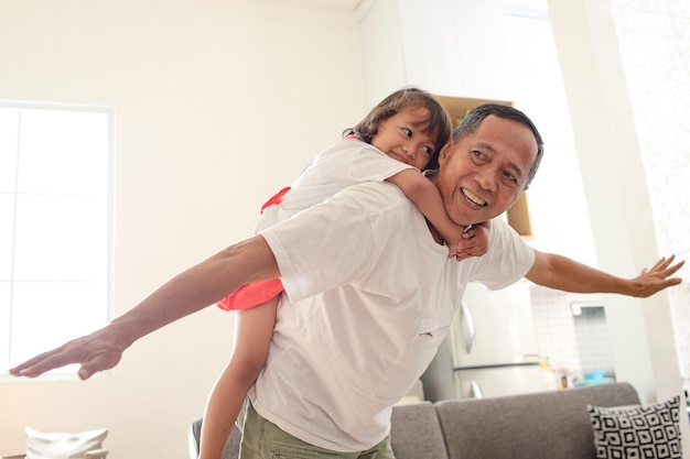 Grandfather carrying his granddaughter on his back playing like a plane at home