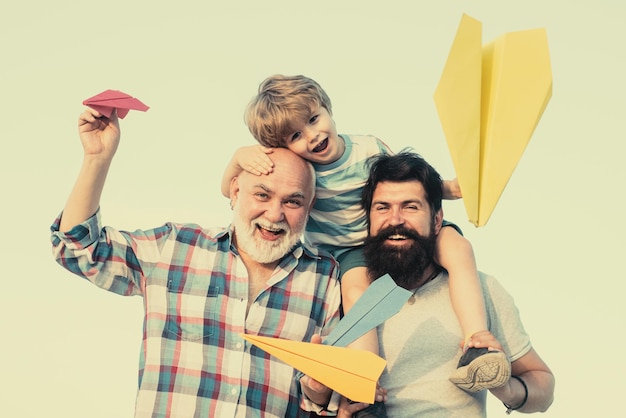 Photo grandfather father and son are hugging and having fun together kid pilot with toy jetpack against sk