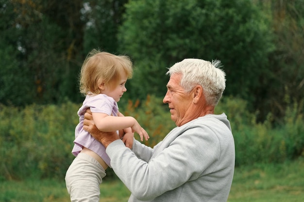 Grandfather and grandchild baby have fun during walk In Park Happy family Old man grandpa hugging 2 years child girl at summer day Smiling Senior male spending time with his granddaughter together