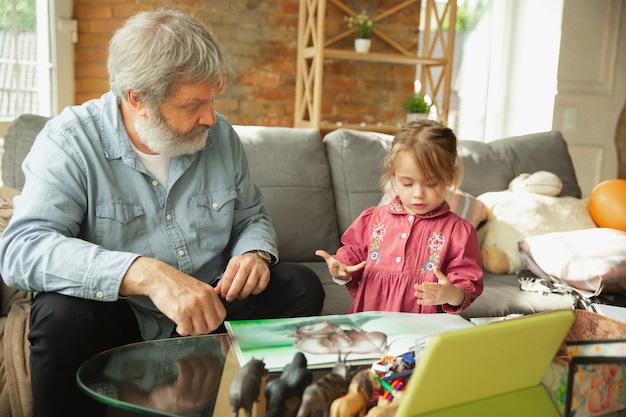 Grandfather and grandchild playing together at home. Happiness, family, relathionship, learning and education concept. Sincere emotions and childhood. Reading books, fairytails, poems, look happy.