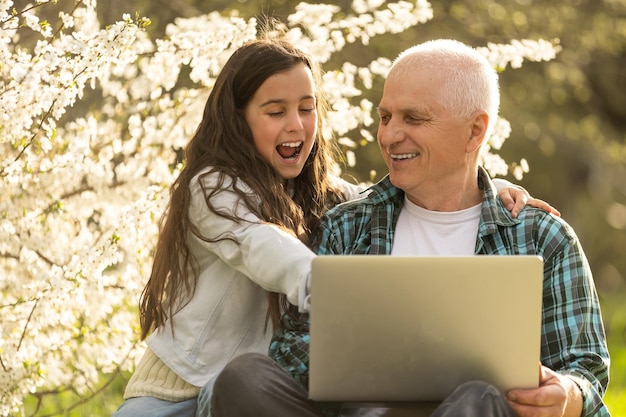 grandfather and granddaughter with laptop in the garden.