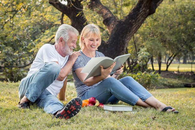 Grandfather and grandmother read a book sitting on the grass.