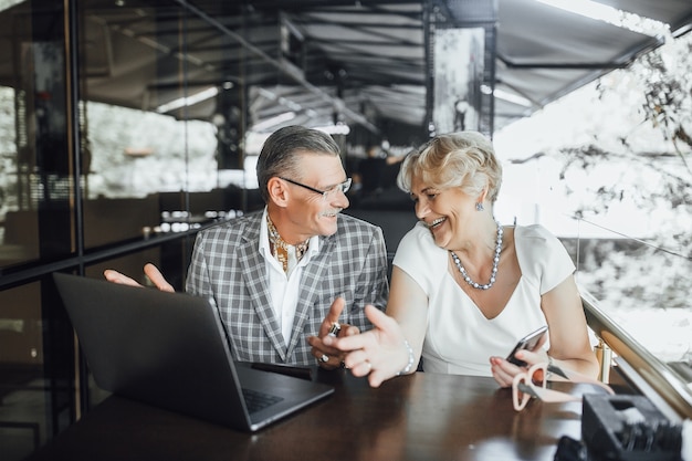 Grandfather and grandmother with eyeglasses sitting in cafe of open laptop computer and smiling