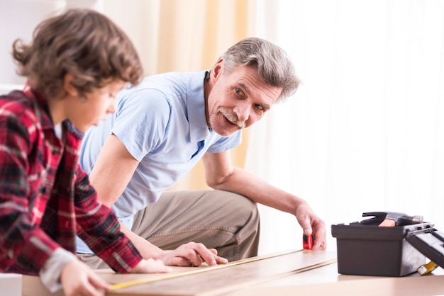 Photo grandfather and grandson are measuring a table.