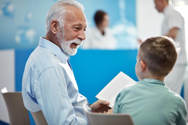 Grandfather and grandson communicating while sitting in hospital hallway Focus is on senior man