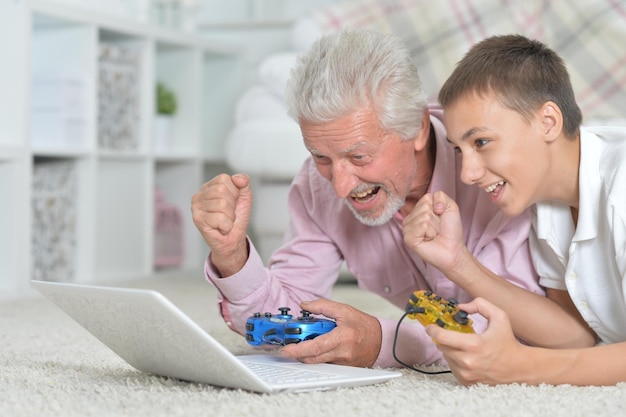 Grandfather and grandson lying on floor and playing computer games on laptop