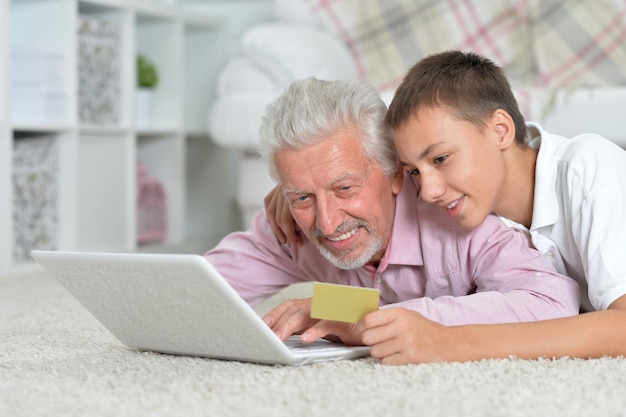 Grandfather and grandson using laptop grandson holding credit c