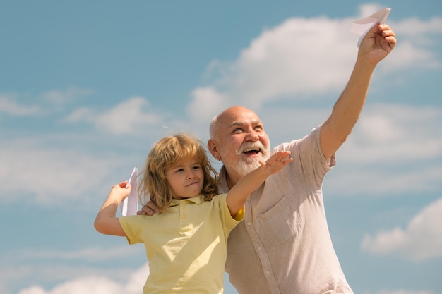 Grandfather and grandson with paper plane over blue sky and clouds Men generation granddad and grand