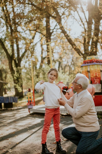 Grandfather having fun with his cute little granddaughter in the amusement park