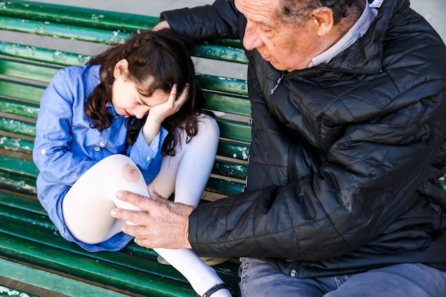 写真 祖父がベンチで孫娘の膝を傷つけた姿を見ている