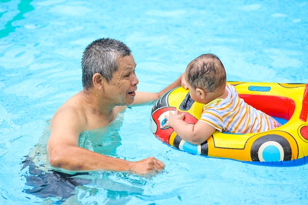 スイミング プールでかわいい男の子と遊ぶおじいちゃん