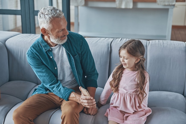 Nonno che mostra lo smartphone alla sua nipotina mentre trascorrono del tempo a casa insieme