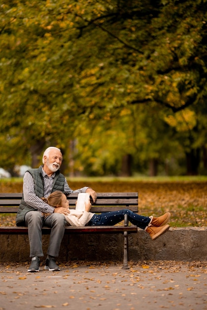 Photo grandfather spending time with his granddaughter on bench in park on autumn day