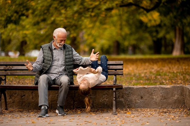 Grandfather spending time with his granddaughter on bench in park on autumn day