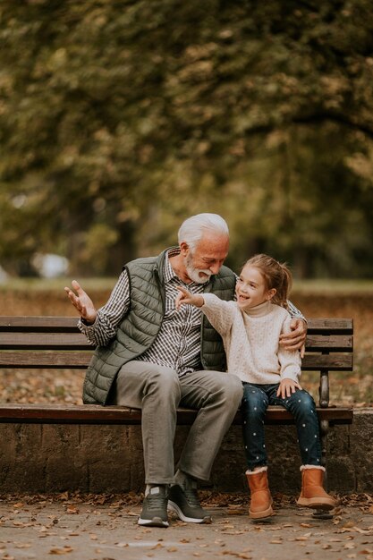 Grandfather spending time with his granddaughter on bench in park on autumn day