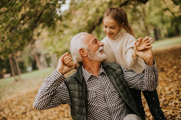 Grandfather spending time with his granddaughter in park on autumn day