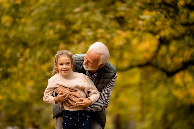 Grandfather spending time with his granddaughter in park on autumn day