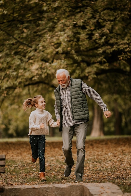 Grandfather spending time with his granddaughter in park on autumn day