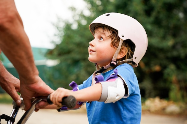 Дедушка учит маленького ребенка кататься на велосипеде Малыш в защитном шлеме учится ездить на велосипеде