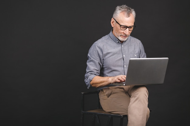 Grandfather using modern technologies. Smiling old businessman in eyeglasses using laptop computer 