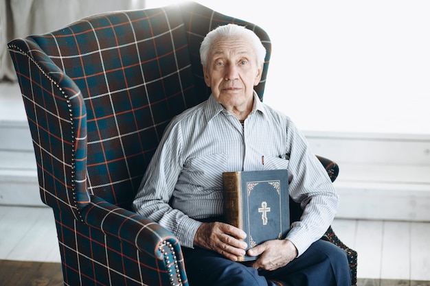 Foto il nonno con la bibbia si siede su una sedia