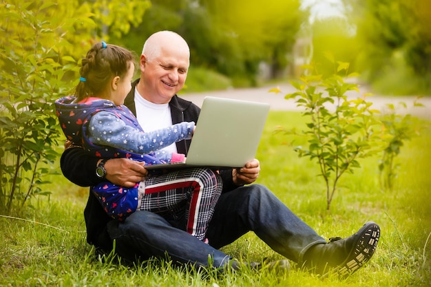 Grandfather with granddaughter. Girl teaching her grandfather. Using laptop.