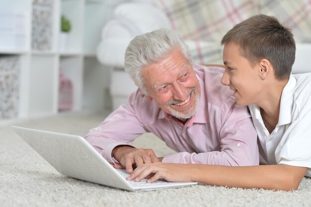 Grandfather with grandson using laptop while lying on floor at home