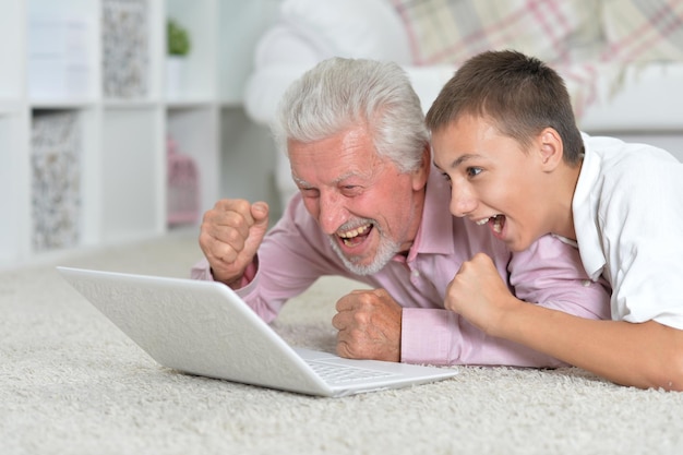 Grandfather with grandson using laptop while lying on floor