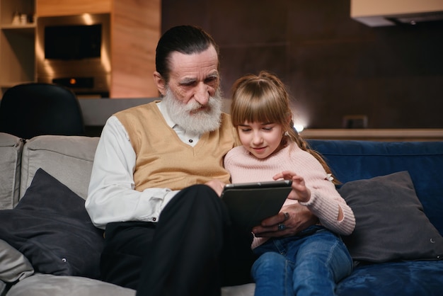 Grandfather with his granddaughter using tablet at home