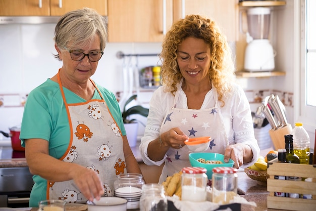 Grandma and daughter at home cooking and smiling - enjoying and have fun indoor together - daughter drinking the and grandma is showing how to cook fish