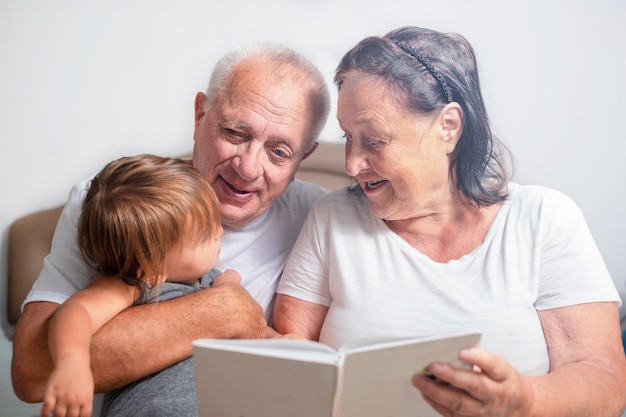 Grandma and grandfather are reading a book to a child. Senior spend time with great granddaughter