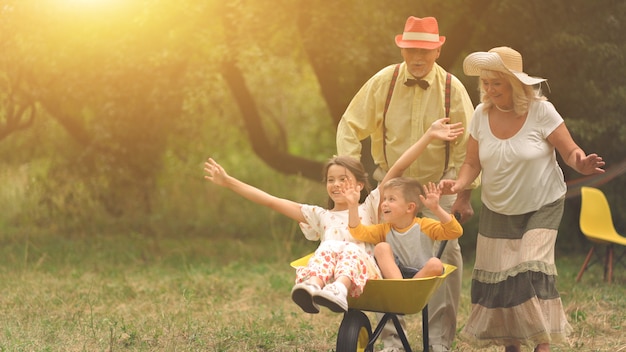 Grandma and grandpa are pushing their grandchildren in a wheelbarrow