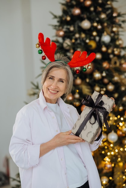 Бабушка в рождественской шапке с оленями, рождественский подарок в руке