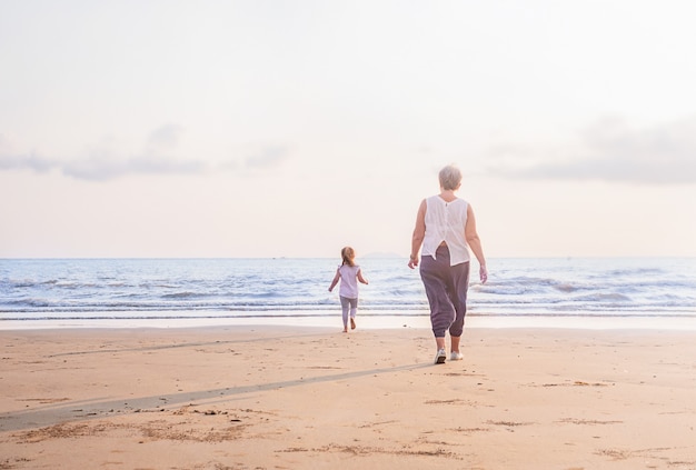 The grandmother and the child are walking along the beach at sunset. The girl runs away from woman to the water