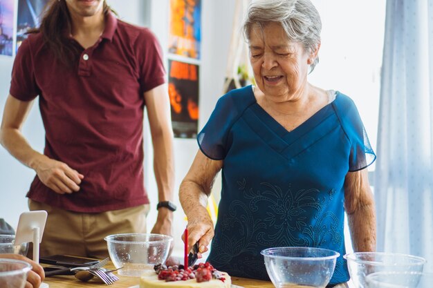 Grandmother cutting the birthday cake in the company of a grandson to start handing it out to others