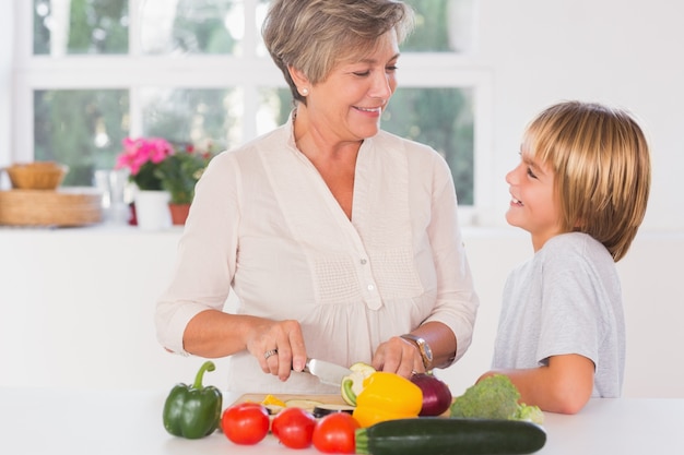 Grandmother cutting vegetables looking at her grandson