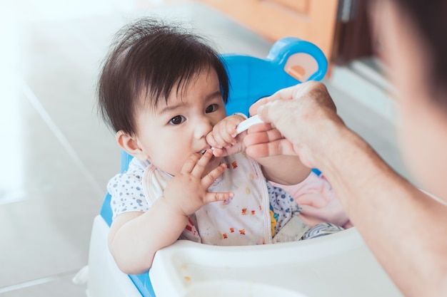 Grandmother feeding cute asian baby girl with a spoon at home. 