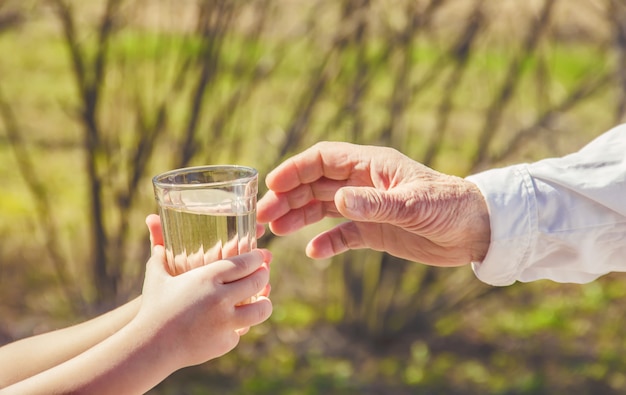 祖母は子供に一杯のきれいな水を与えます。セレクティブフォーカス