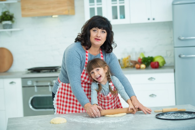 Grandmother and granddaughter cook pizza together, roll the dough with a rolling pin. Family culinary traditions.