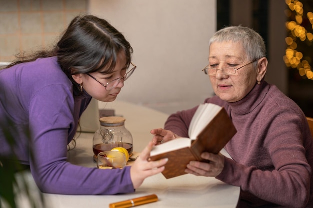 La nonna e la nipote bevono il tè si siedono al tavolo e leggono un libro messa a fuoco selettiva